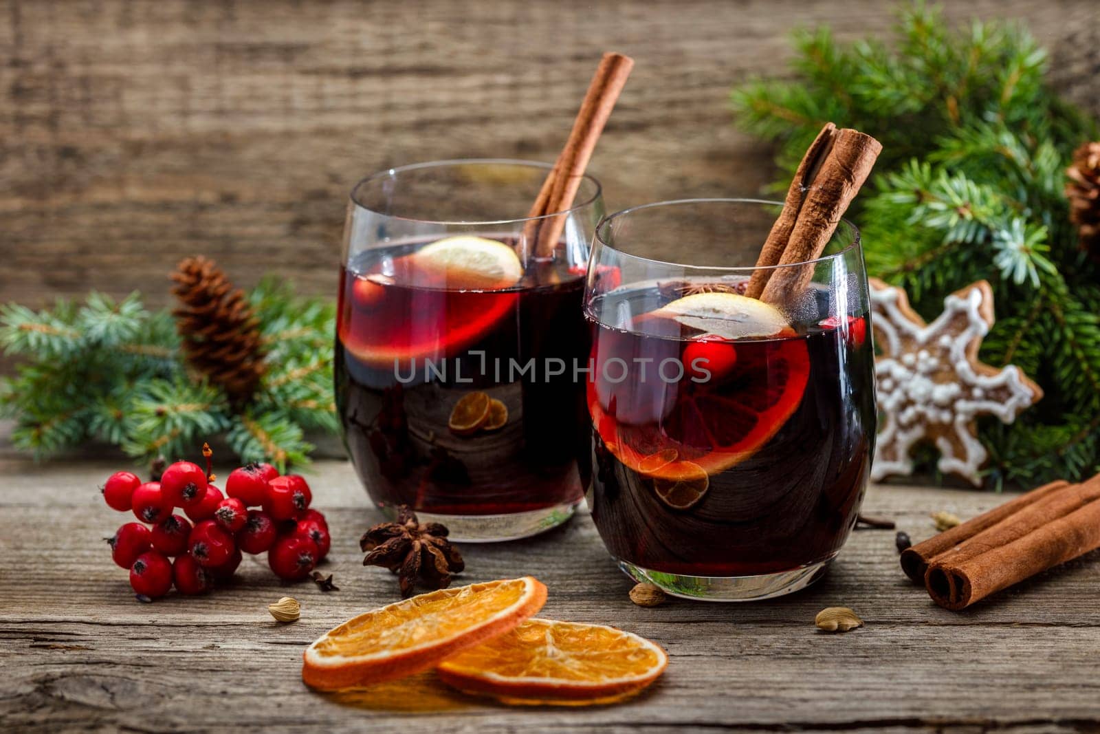 Mulled wine in glasses in a Christmas setting with dry slices of oranges, cookies in the shape of a snowflake, red berries and cinnamon