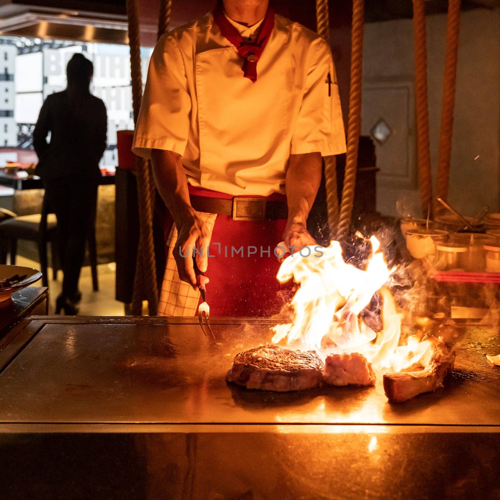 Cooking of beef teppanyaki recipe japanese grilled beef tomahawk steak on cooking pan using scraper with flame in background