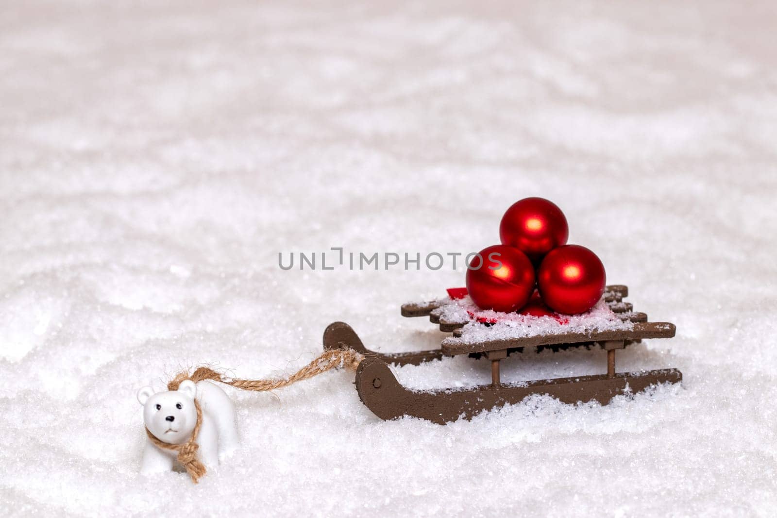 Christmas greeting card template. A little polar bear pulls a sleigh with three red Christmas balls through the snow. Copy space for your design. Macro photograph.