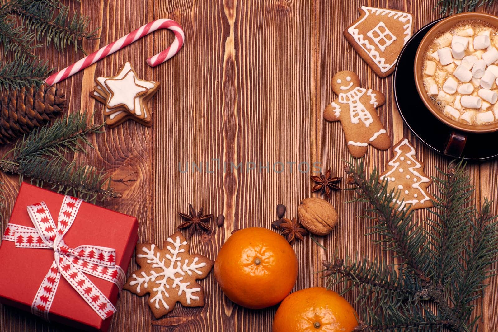 Christmas decor with fir tree branches, glass mug with hot cocoa and marshmallow, gingerbreads and gift box on a wooden background with copy space for text. Top view. For greeting card.