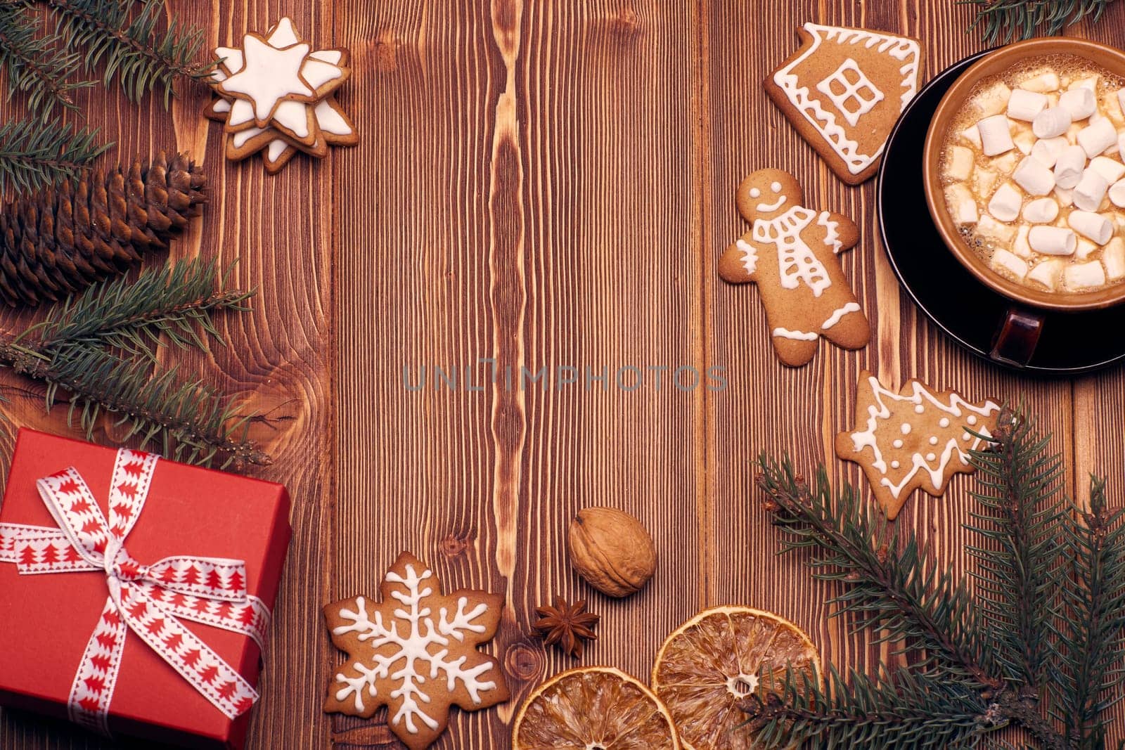 Christmas decor with fir tree branches, glass mug with hot cocoa and marshmallow, gingerbreads and gift box on a wooden background with copy space for text. Top view. For greeting card.