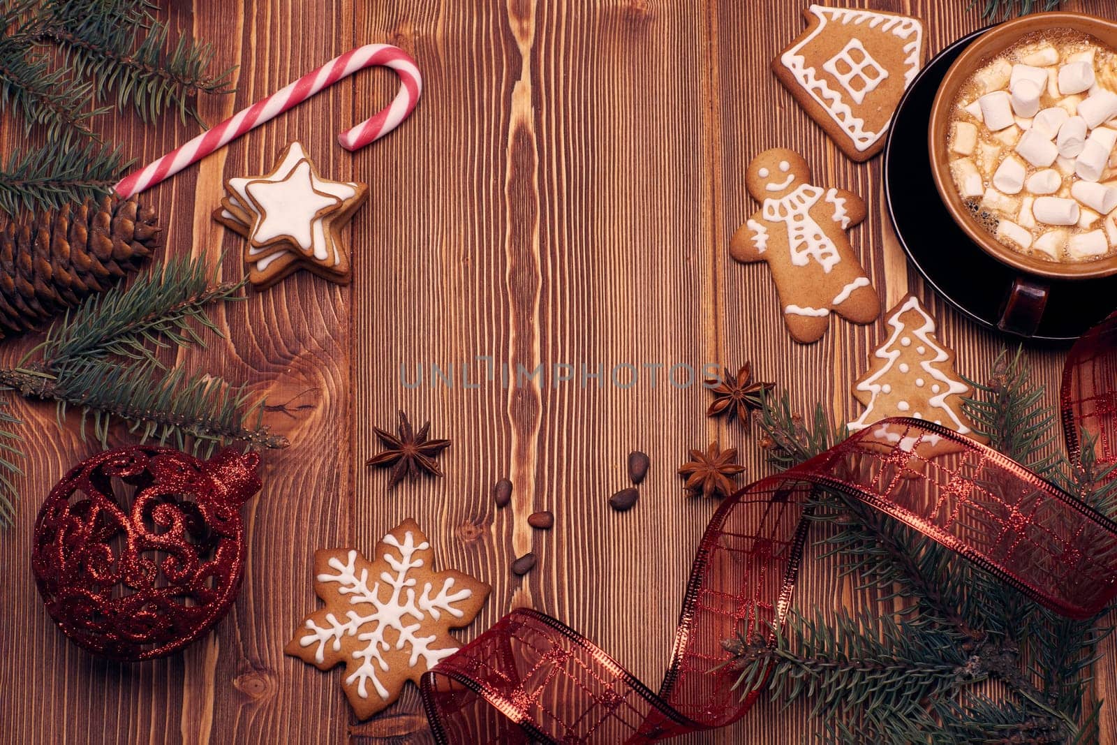 Christmas decor with fir tree branches, glass mug with hot cocoa and marshmallow, gingerbreads and gift box on a wooden background with copy space for text. Top view. For greeting card.