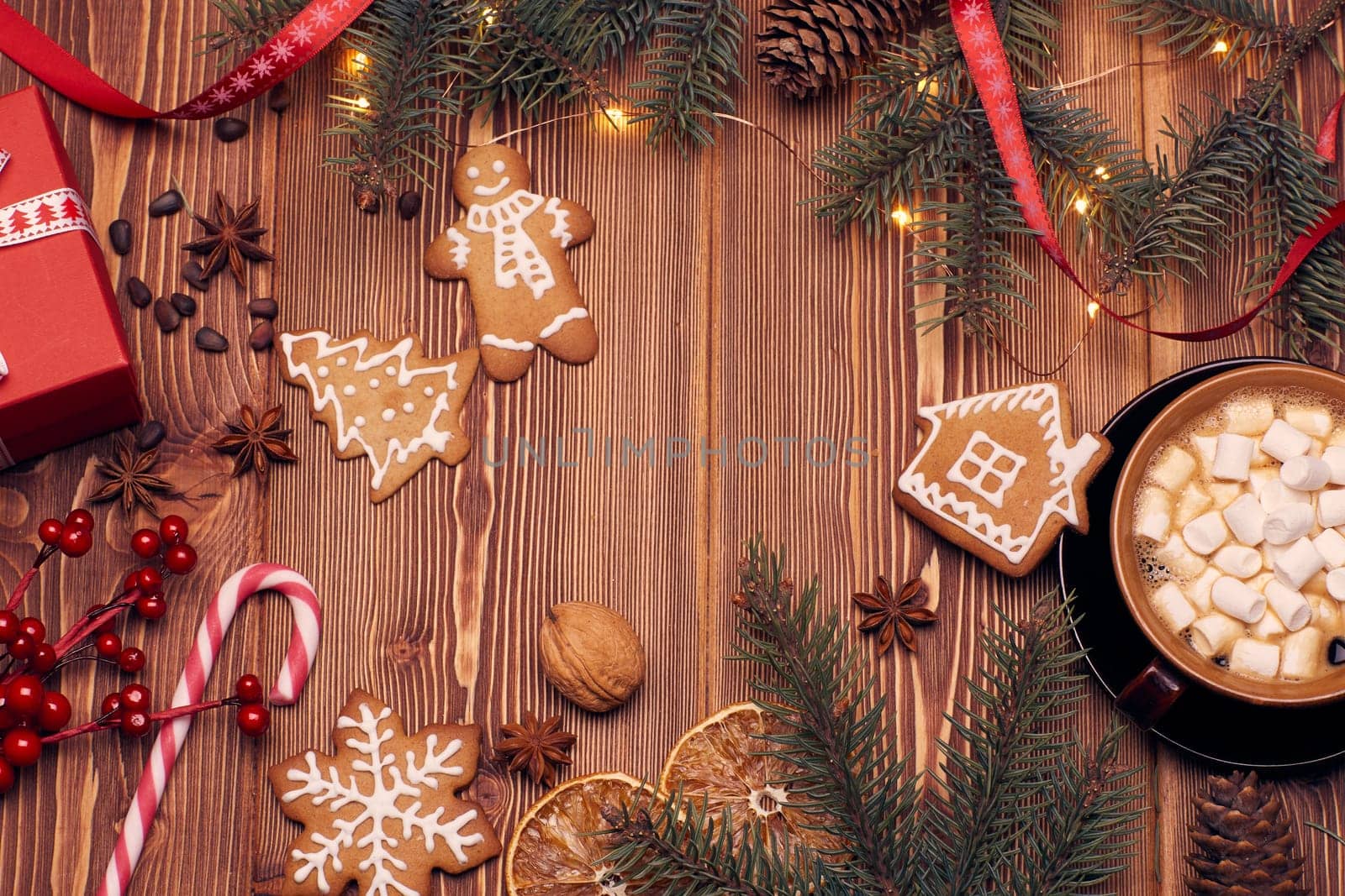 Christmas decor with fir tree branches, glass mug with hot cocoa and marshmallow, gingerbreads and gift box on a wooden background with copy space for text. Top view. For greeting card.