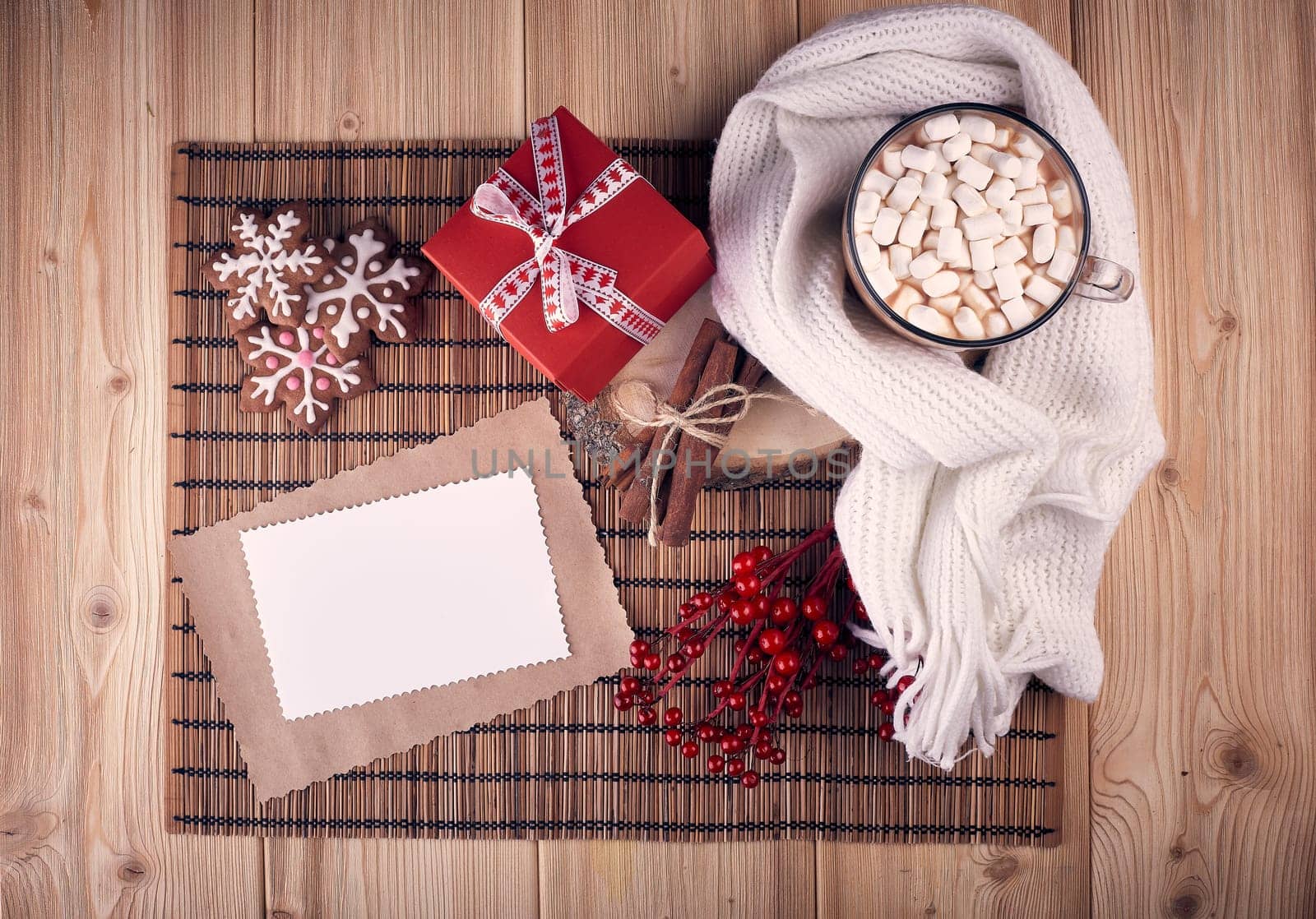 Glass mug with hot cocoa and marshmallow, gingerbread, gift box and blank sheet for text on wooden background. Mockup. Top view. Christmas and New Year greeting card.