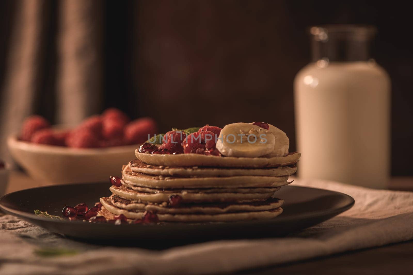 Pancakes with raspberries, banana slices, pomegranate seeds and honey on wooden vintage table.