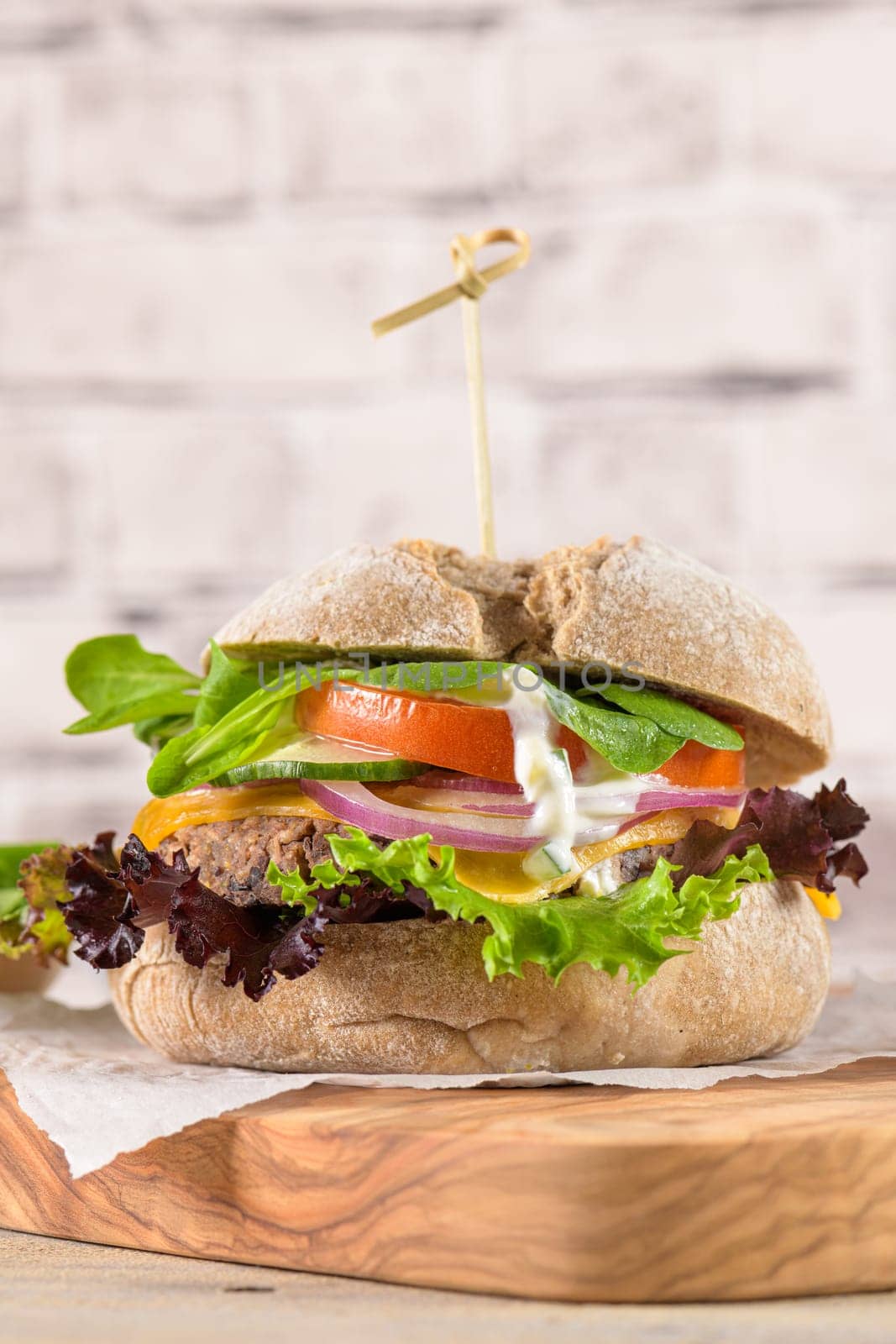 Healthy vegan burger with fresh vegetables and yogurt sauce on rustic kitchen counter top.