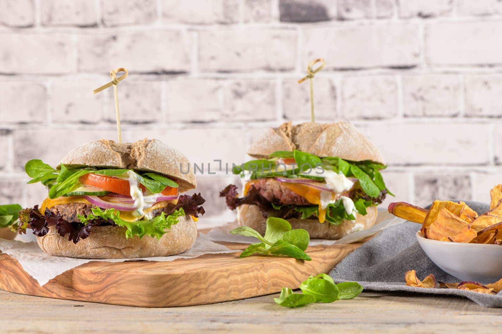 Healthy vegan burger with fresh vegetables and yogurt sauce on rustic kitchen counter top.