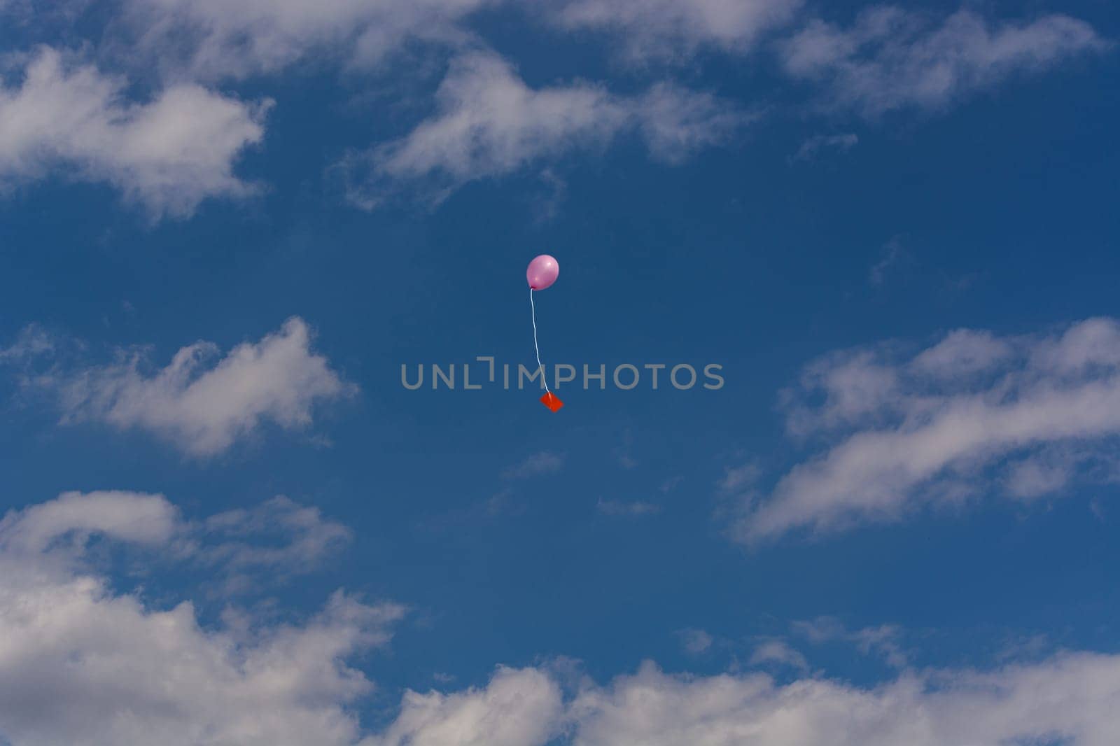 Pink balloon with ribbon and greeting card in front of blue sky