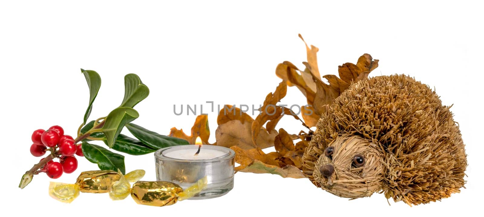 Christmas decoration with autumn leaves, candle and straw hedgehog in front of white background