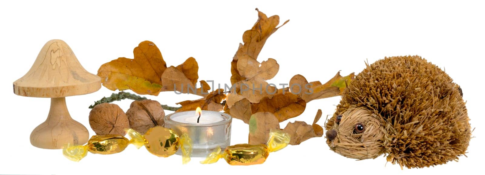Christmas decoration with autumn leaves, candle, wooden mushroom and straw hedgehog in front of white background