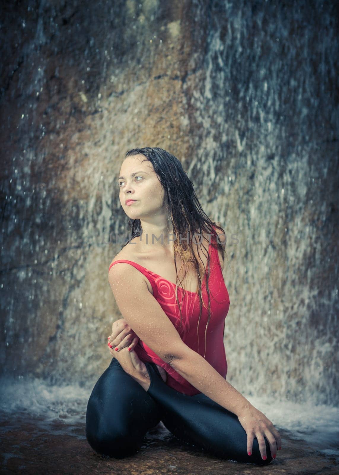 Woman practicing yoga near waterfall. Twisted lotusl Pose. Bharadvajasana