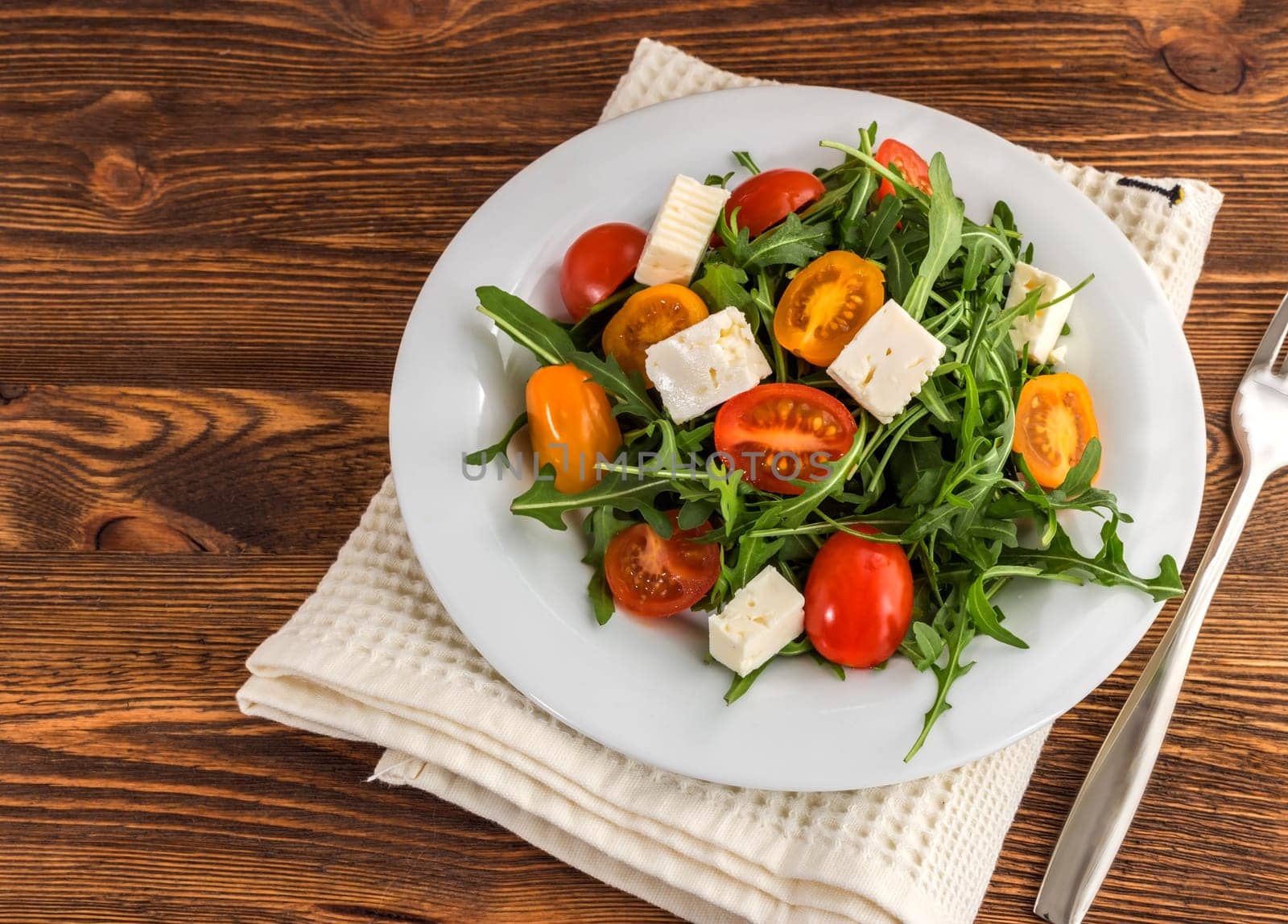light salad of arugula, tomatoes and feta cheese on a wooden background