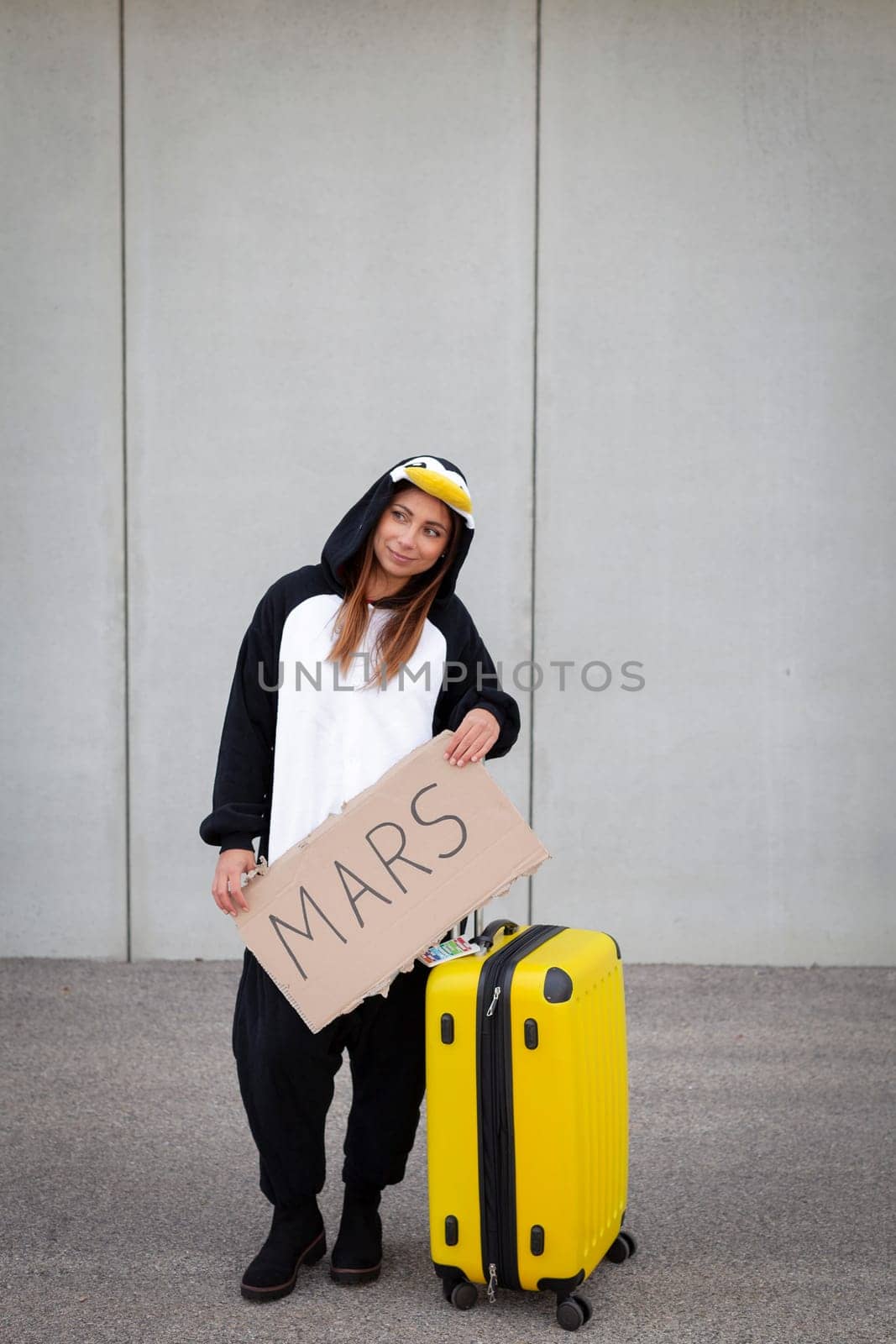 Young woman, with penguin costume and yellow suitcase, has to travel due to global warming. Symbolizes a sad penguin who has to leave his homeland because of global warming or climate change.