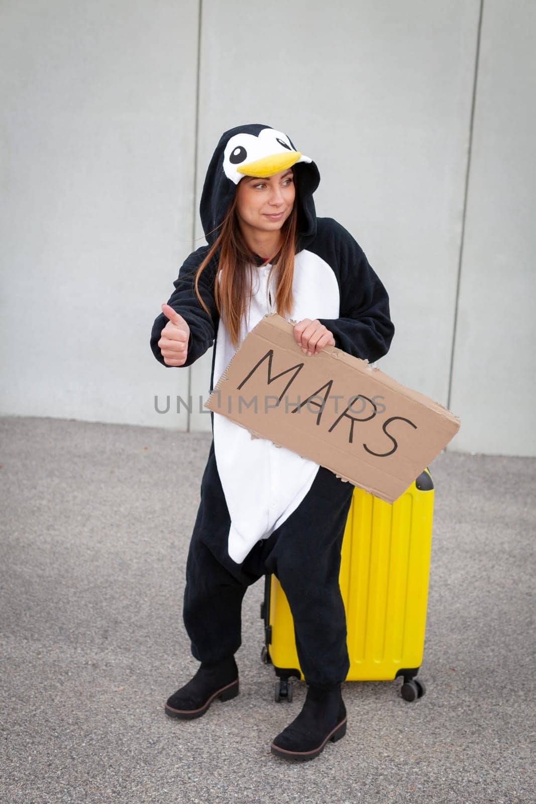 Young woman, with penguin costume and yellow suitcase, has to travel due to global warming. Symbolizes a sad penguin who has to leave his homeland because of global warming or climate change.