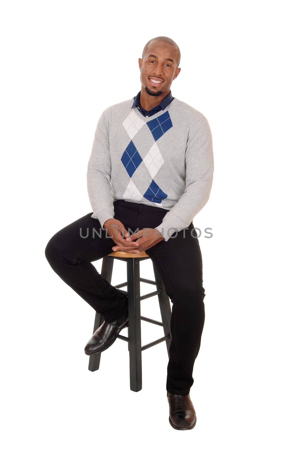 A young handsome African American man sitting full body in the.studio, thinking and smiling, isolated for white background.