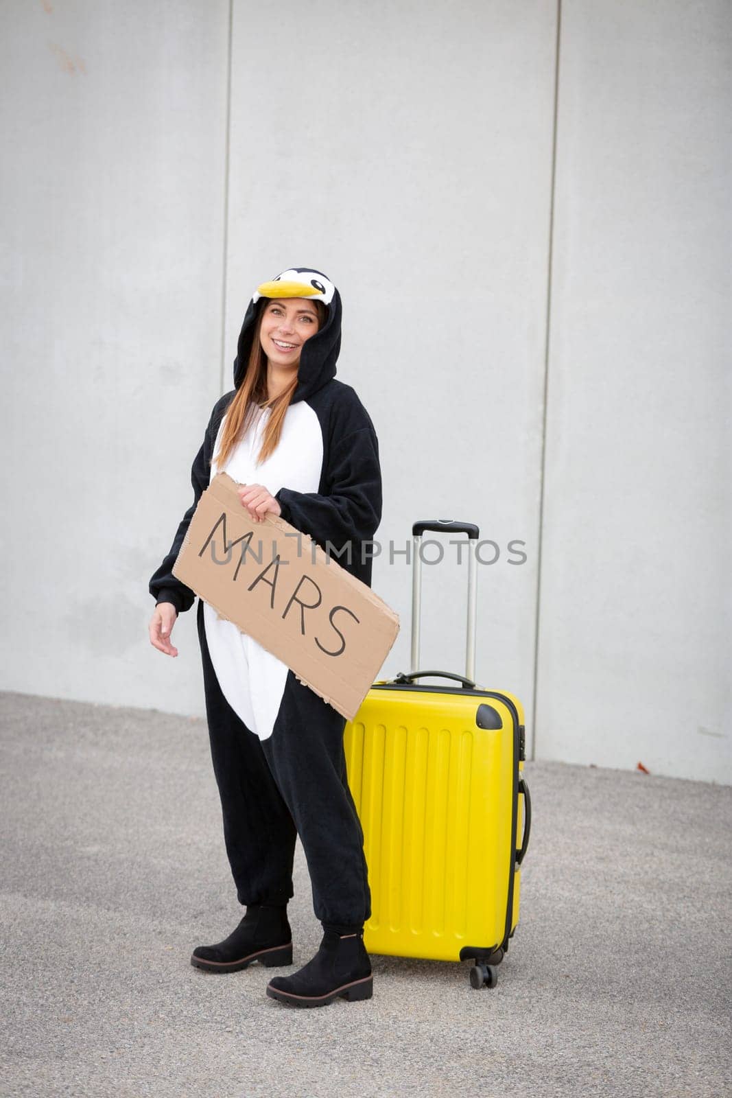 Young woman, with penguin costume and yellow suitcase, has to travel due to global warming. Symbolizes a sad penguin who has to leave his homeland because of global warming or climate change.
