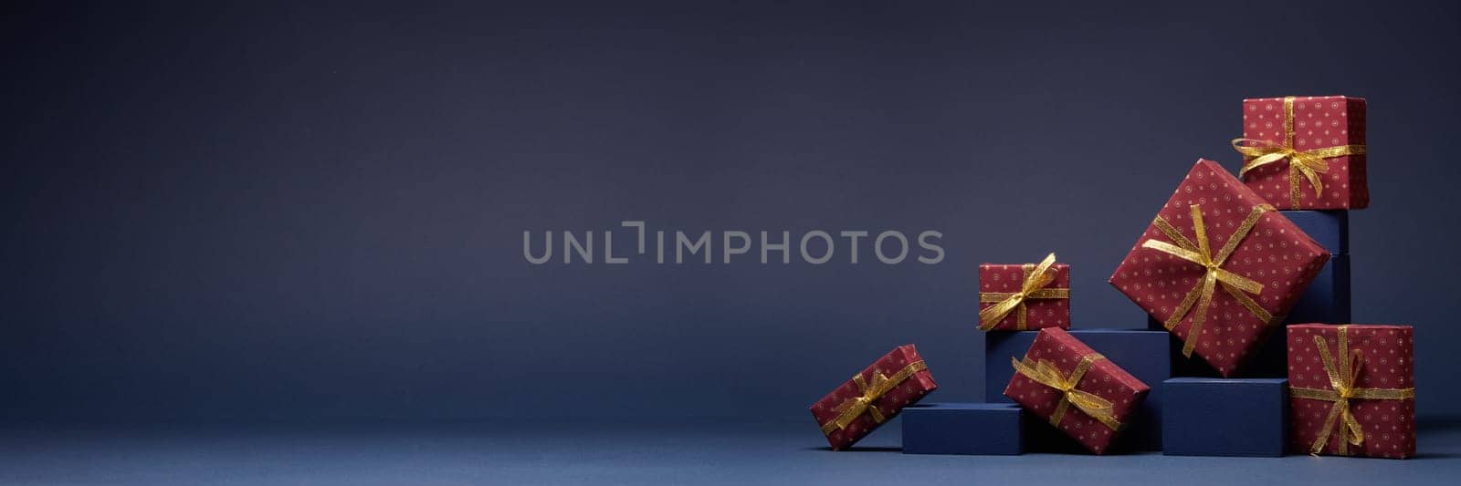 Composition with blue geometric figures and red gift boxes with golden ribbon on dark blue background with copy space. Christmas. New Year. Shopping. Sale. For design of advertising, greeting card