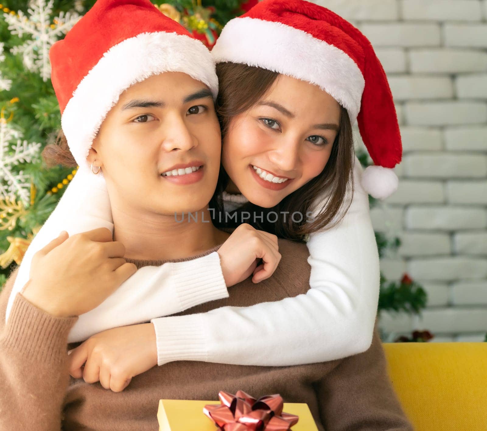 Young asian adult teenager couple hugging and  celebrateing christmas holiday together in living room with christmas tree decoration.