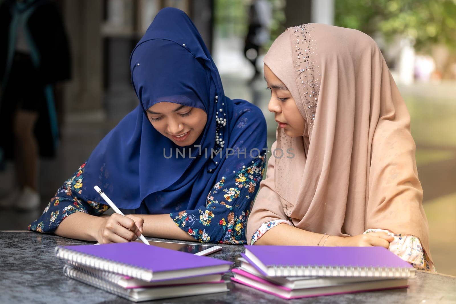 Teenager Young Adult Asian Thai Muslim university college students reading book and using digital tablet together using for education and online education concept