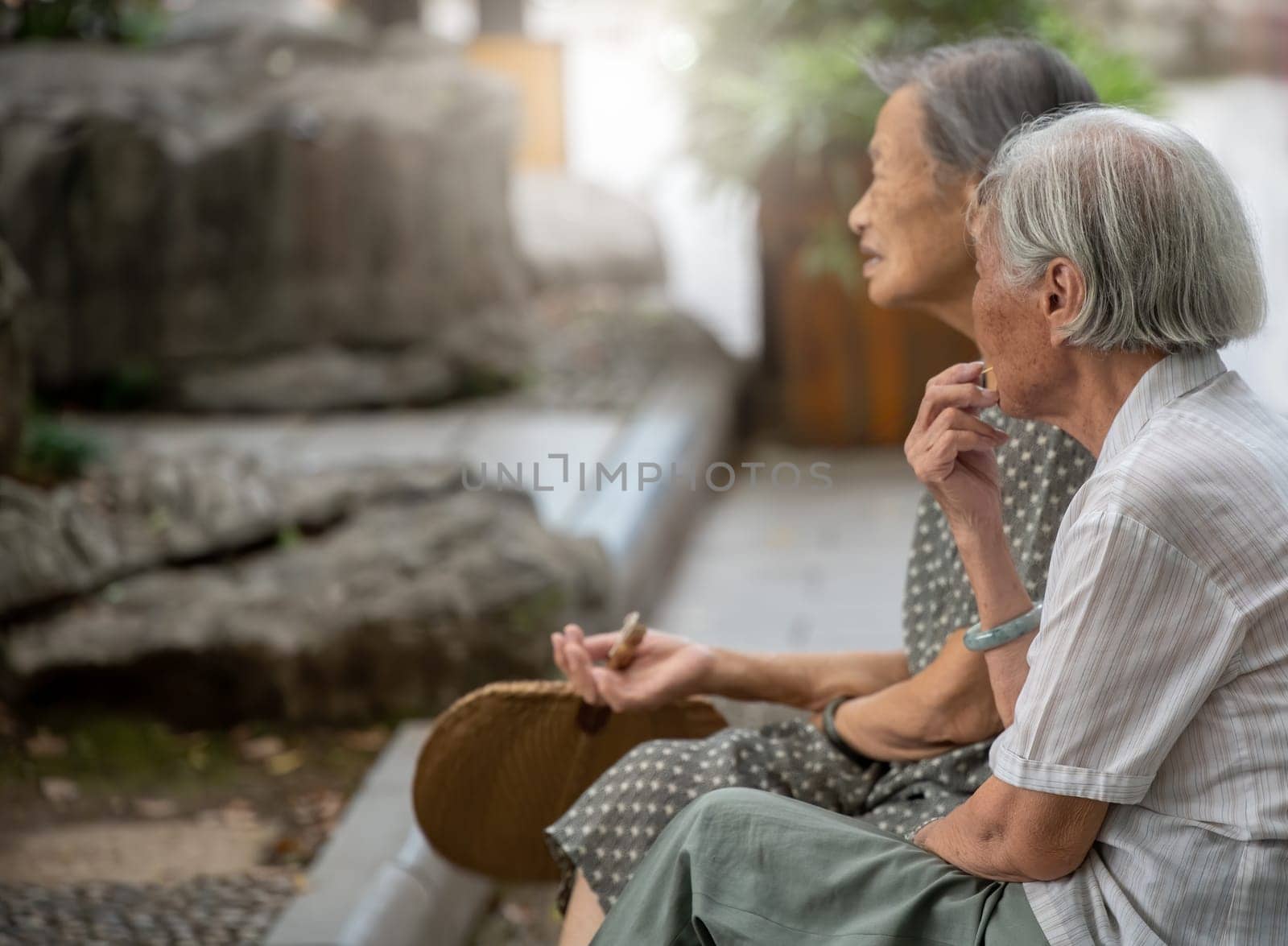 Guilin, China -  August 2019 : Portrait of two old retired chinese asian women sitting on a bench by the Shan Lake in a park  in summer