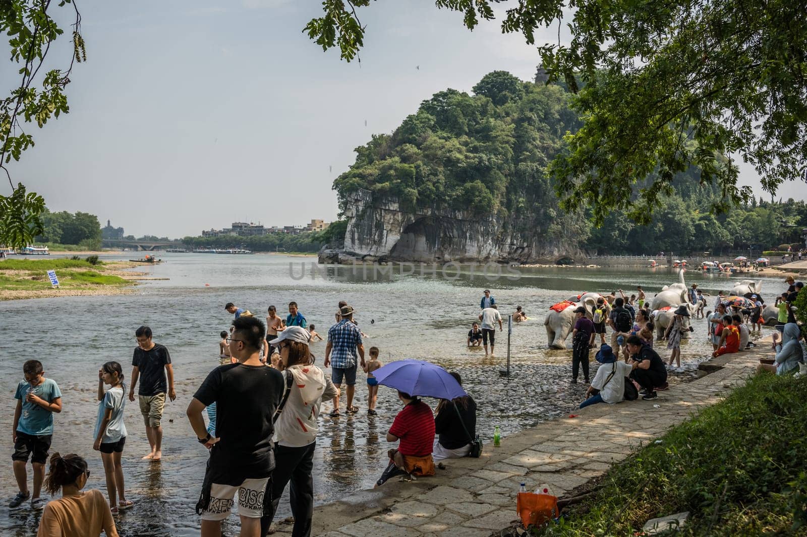 Guilin, China -  August 2019 : Crowds of people on the riverbank in summer in the extremely popular Park with Elephant Trunk Hill Arch and the Li Lijiang River in Guilin, Guangxi Province