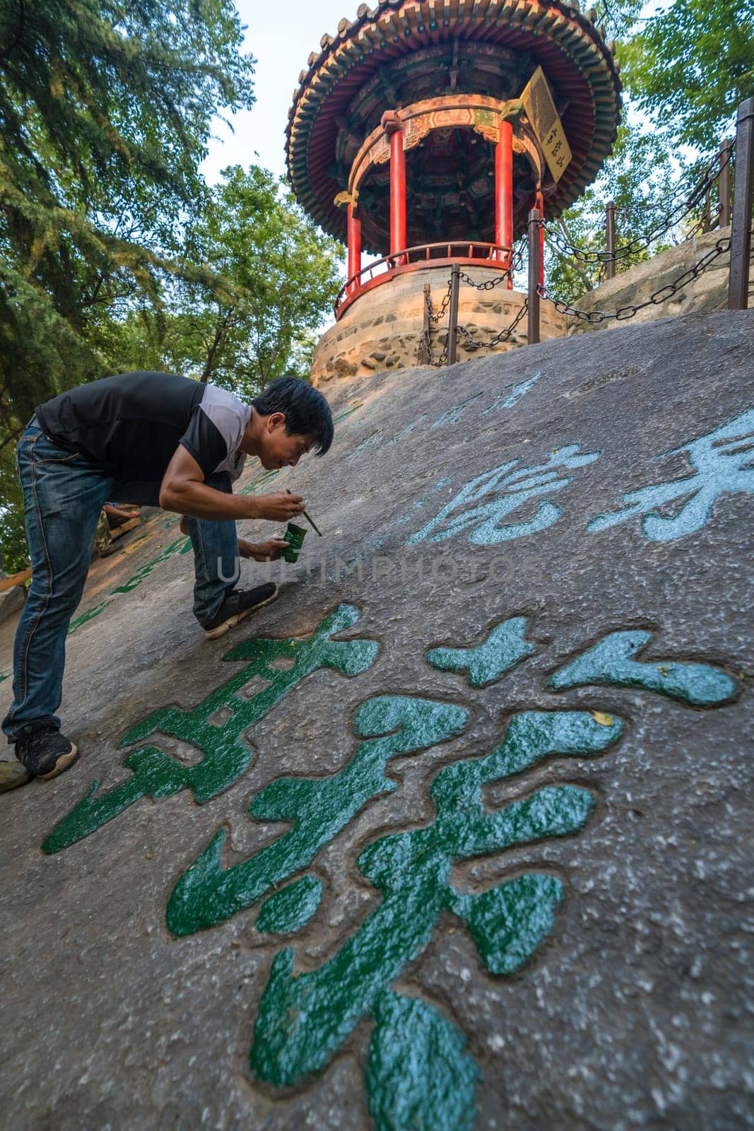 Huashan, China -  August 2019 : Man painting chinese calligraphy characters on a large boulder in the courtyard of a Buddhist temple at the foot of Huashan mountain, Xian, Shaanxi Province