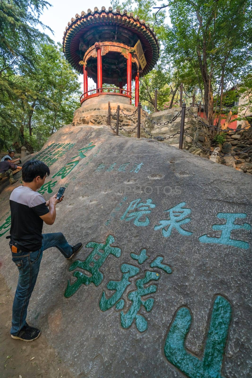 Huashan, China -  August 2019 : Man taking picture of his work on a smartphone after painting chinese calligraphy characters on a large boulder in the courtyard of a Buddhist temple at the foot of Huashan mountain, Xian, Shaanxi Province