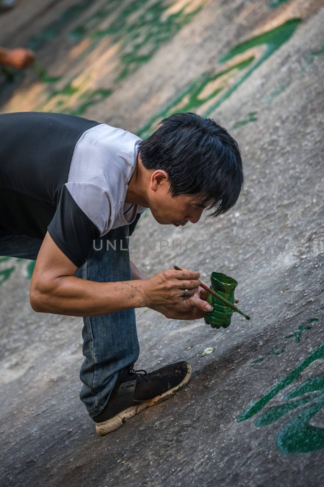 Huashan, China -  August 2019 : Man painting chinese calligraphy characters on a large boulder in the courtyard of a Buddhist temple at the foot of Huashan mountain, Xian, Shaanxi Province