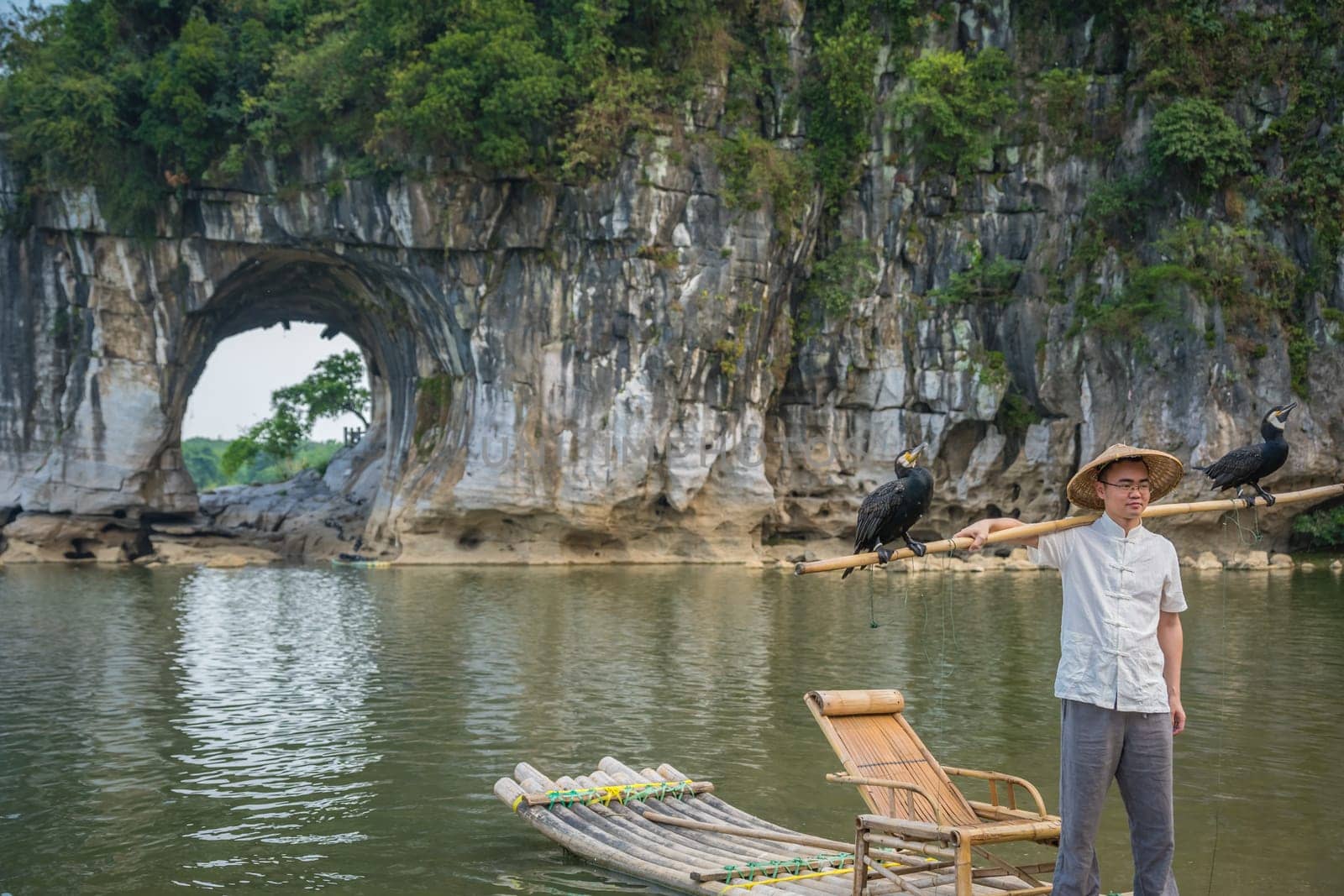 Guilin, China -  August 2019 : Tourist holding bamboo stick with cormorant birds and posing for souvenir photo in front of the landmark Elephant Trunk Hill Arch and the Li Lijiang River, Guangxi Province