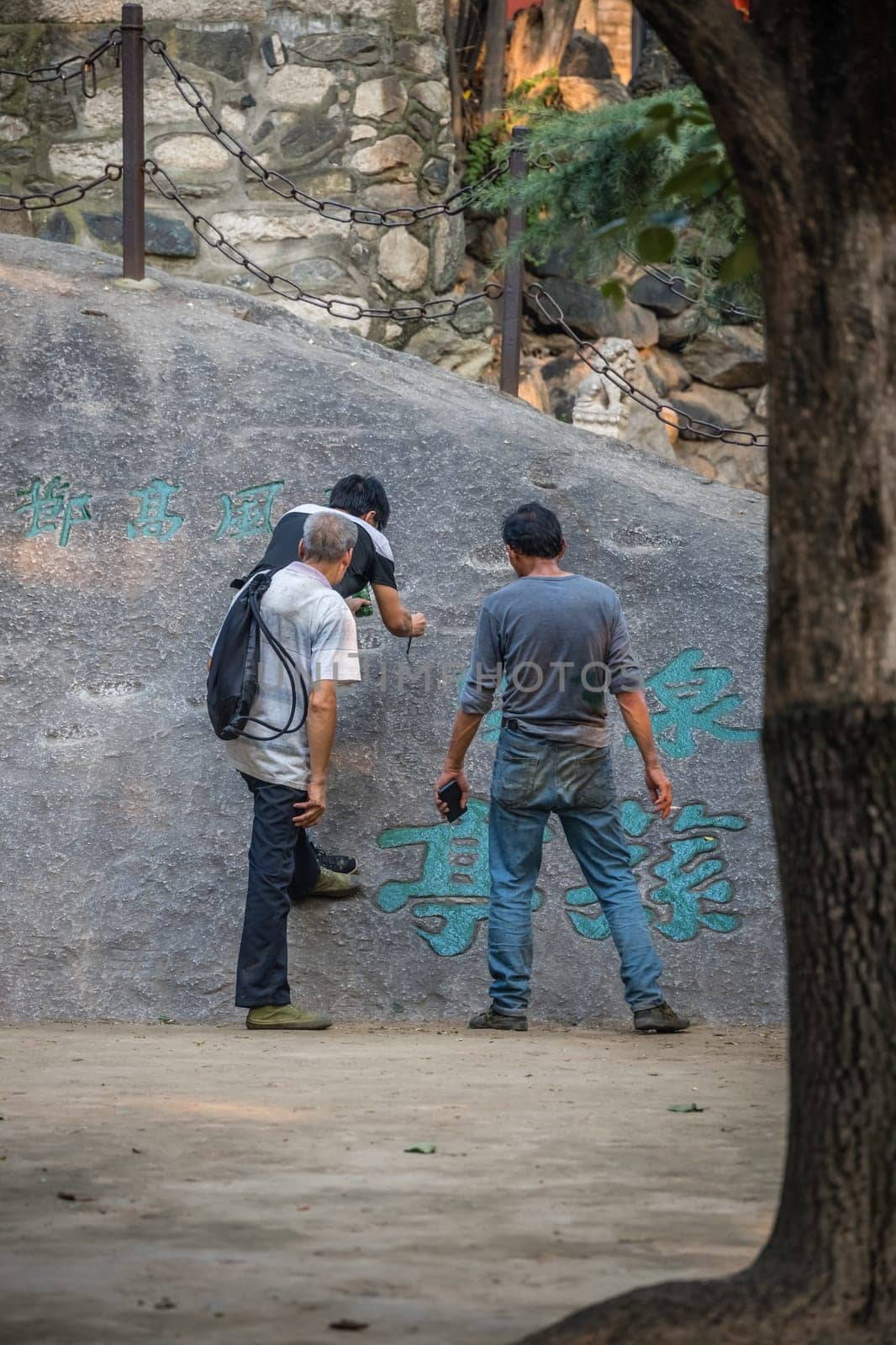 Huashan, China -  August 2019 : Man painting chinese calligraphy characters on a large boulder in the courtyard of a Buddhist temple at the foot of Huashan mountain, Xian, Shaanxi Province