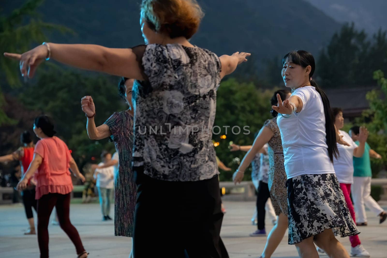 Huashan, China -  August 2019 : Group of Chinese women dancing in the open plaza square at the foot of HuaShan mountain at dusk, Shaanxi Province