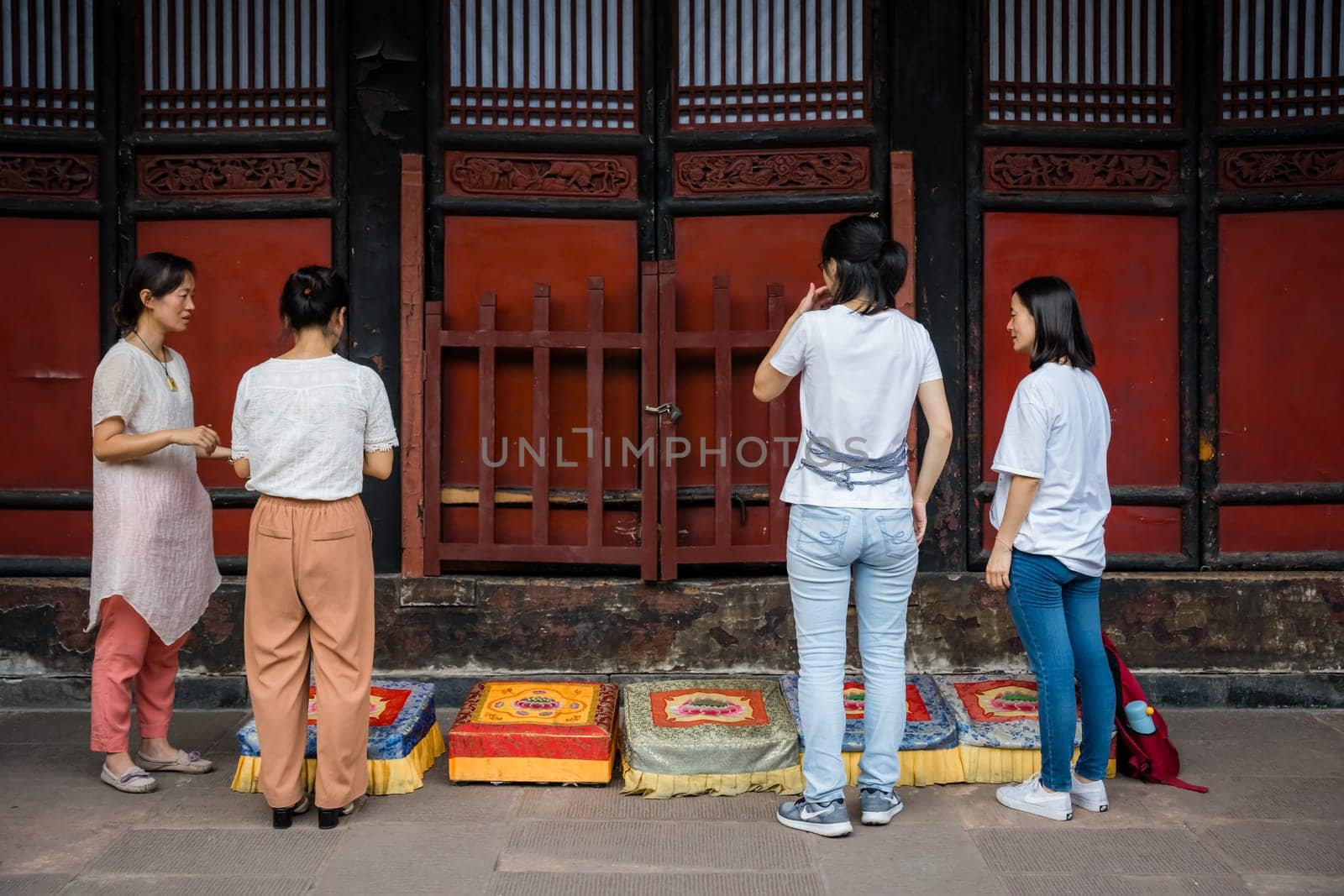 Chengdu, China -  July 2019 :  Four women preparing for a prayer in front of colorful praying kneeling pads in the courtyard of the Buddhist Wenshu Monastery, Sichuan Province