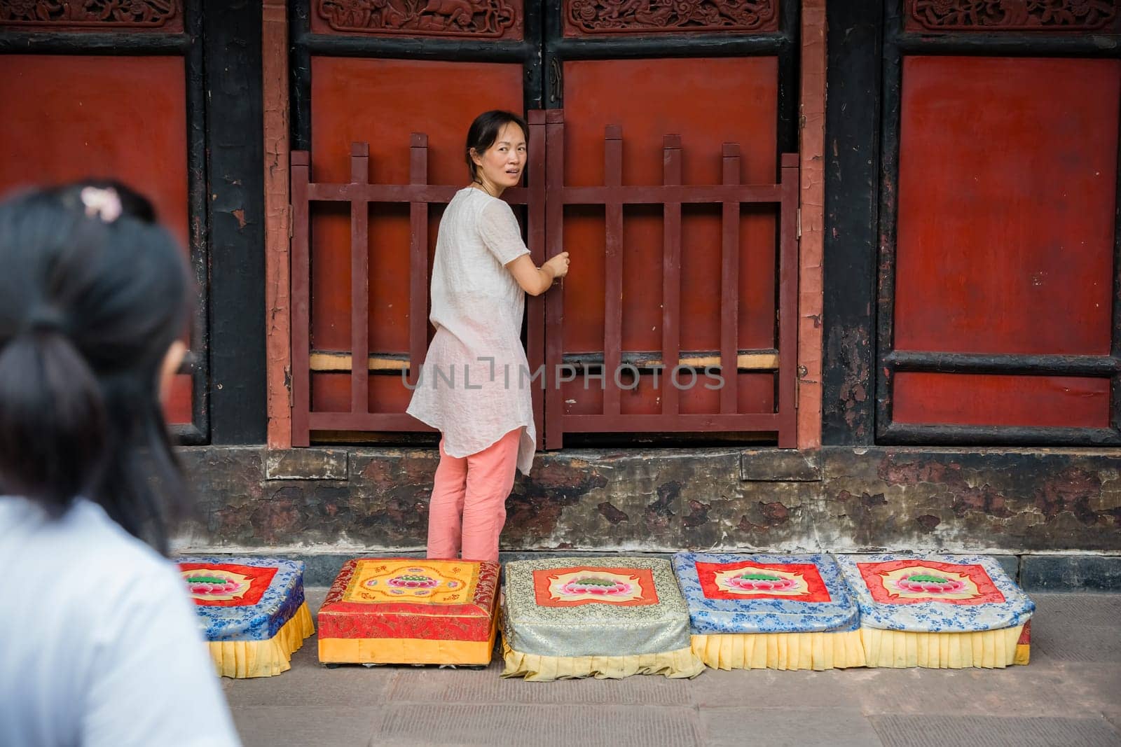 Chengdu, China -  July 2019 :  Chinese woman preparing for a prayer in front of colorful praying kneeling pads in the courtyard of the Buddhist Wenshu Monastery, Sichuan Province