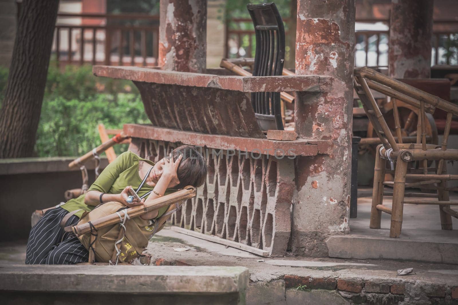 Chengdu, China -  July 2019 : Tired woman sleeping in a wicker chair under pagoda roof in the Chinese garden in the Wenshu Monastery, Sichuan Province