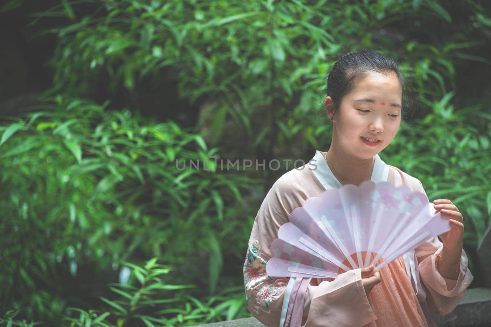 Chengdu, China -  July 2019 :  Portrait of a young asian chinese bride holding a fan at wedding ceremony in the park