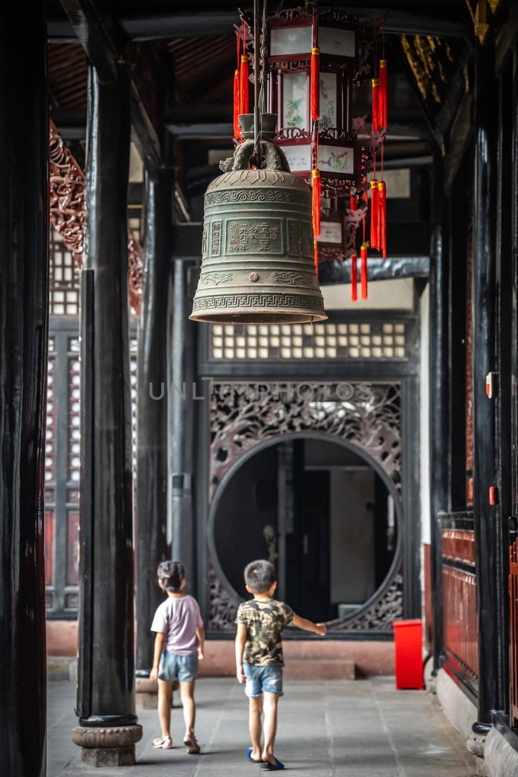 Chengdu, China -  July 2019 : Two little boys walking under the large Brass Bell hanging under the roof in Wenshu Monastery
