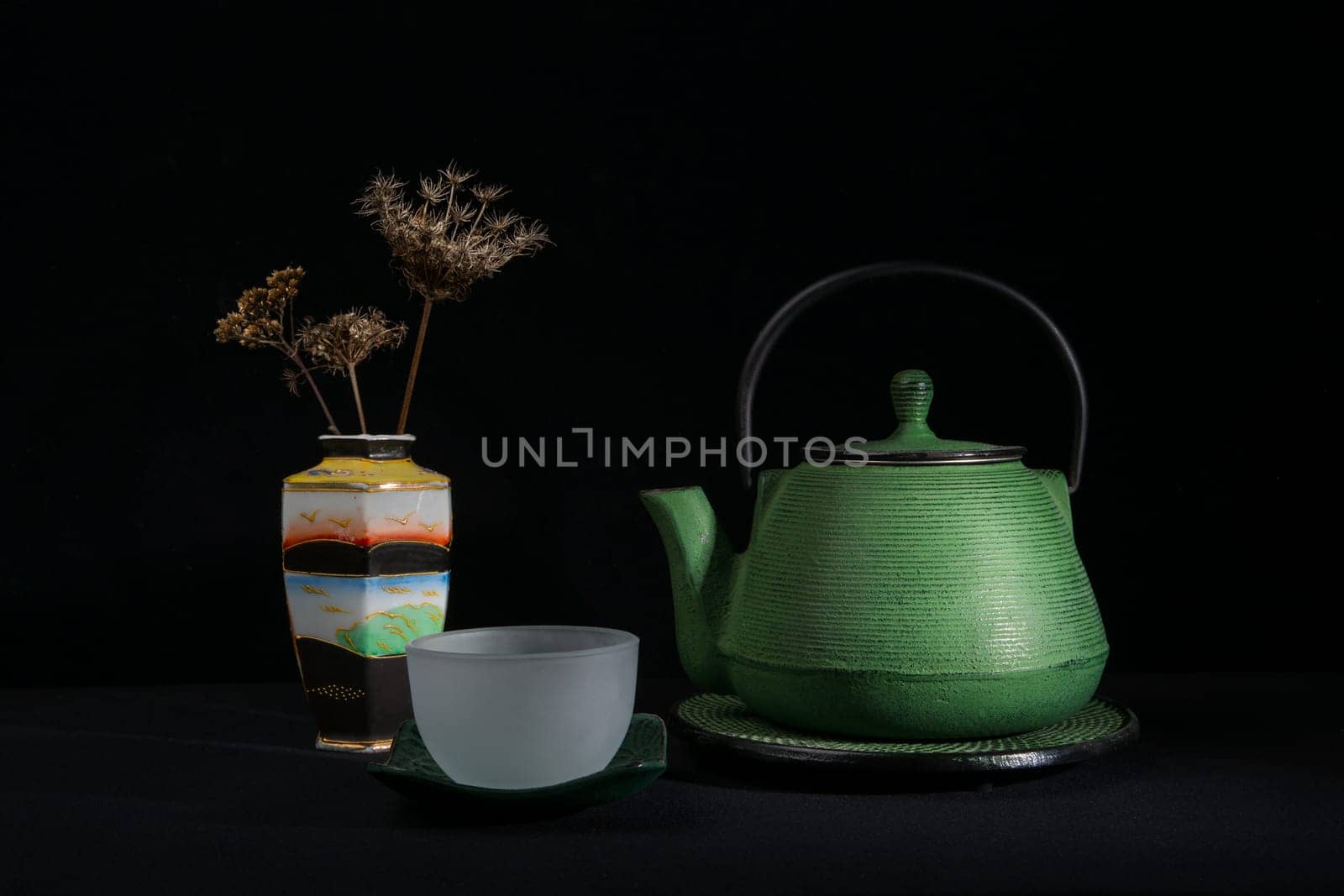 A green metal teapot, a glass bowl and a chinese vase with dried umbels. Isolated on a black background