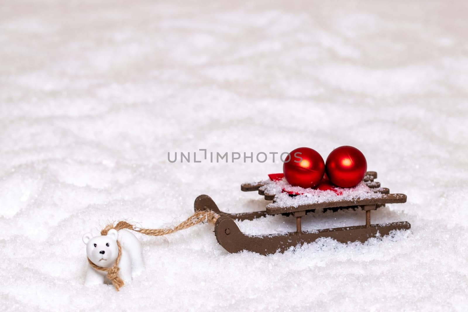 Christmas greeting card template. A little polar bear pulls a sleigh with two red Christmas balls through the snow. Copy space for your design. Macro photograph.