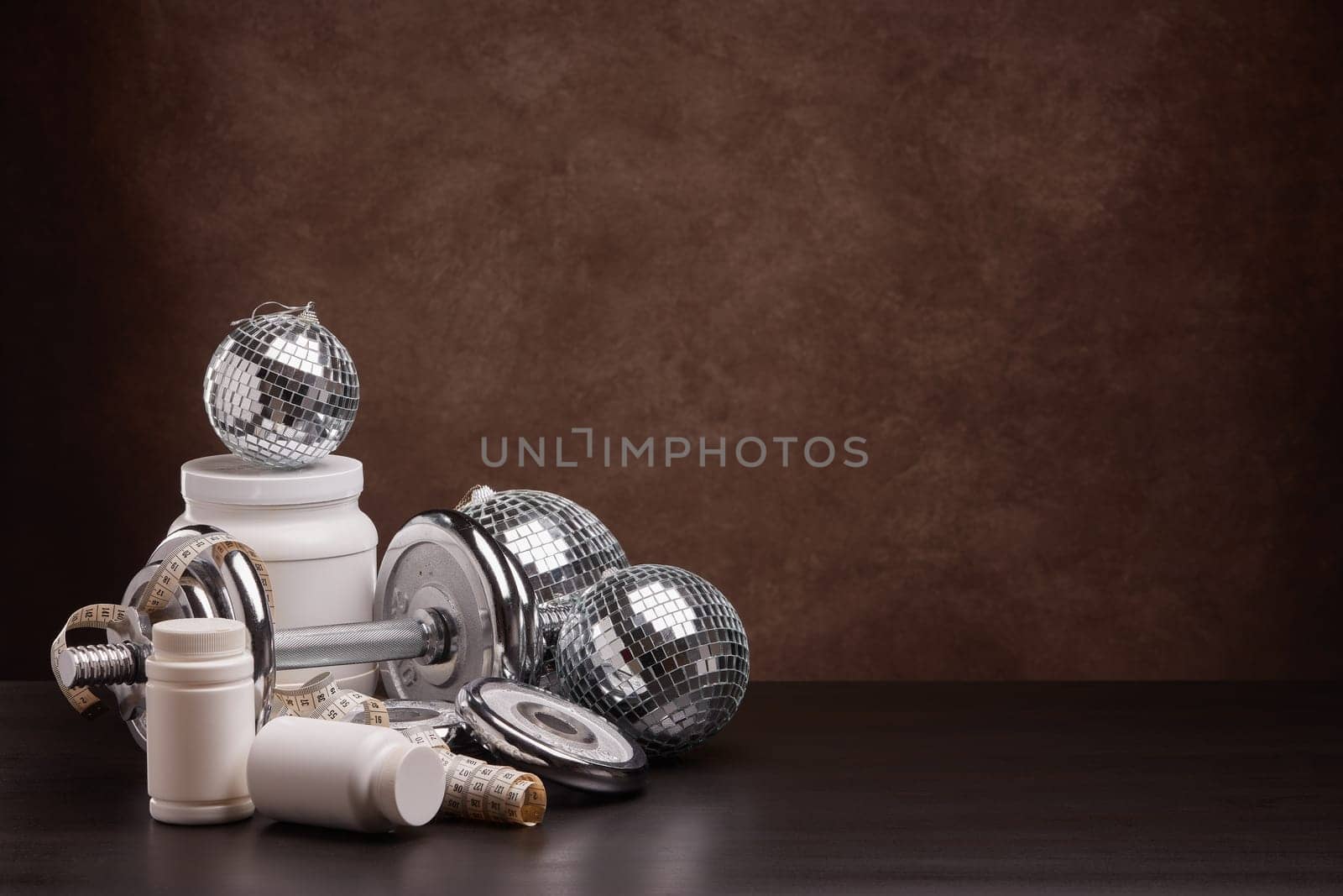 Sports nutrition (supplements), sports equipment and mirror balls on dark brown background with copy space. Fitness, sport or healthy lifestyle concept. New Year and Christmas.