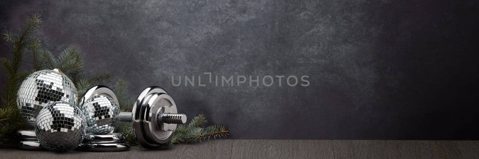 Sports equipment (dumbbell with weights), fir branch, Christmas ornament on dark grey background with copy space. Fitness, sport or healthy lifestyle concept. New Year and Christmas.