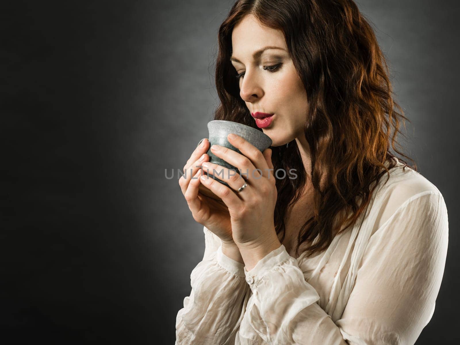 Beautiful happy redhead woman blowing on her hot coffee.