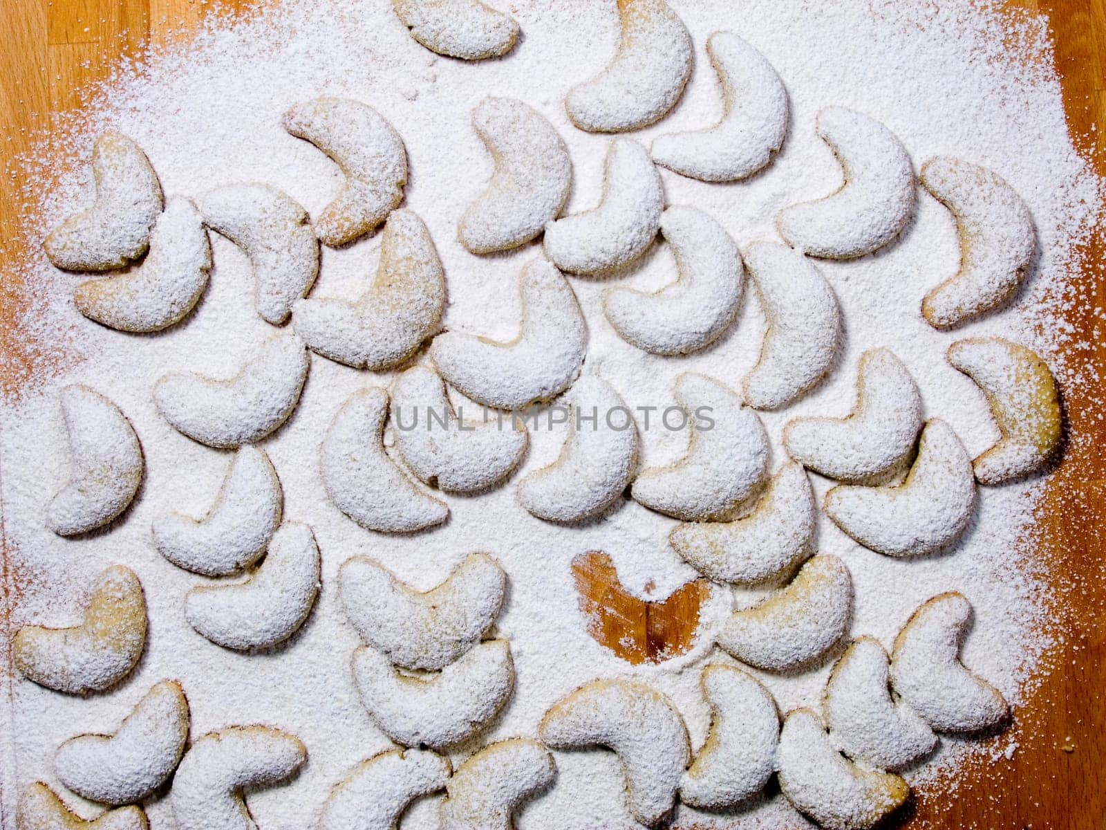 Vanilla crescents covered with powdered sugar on a pastry board with one of them missing