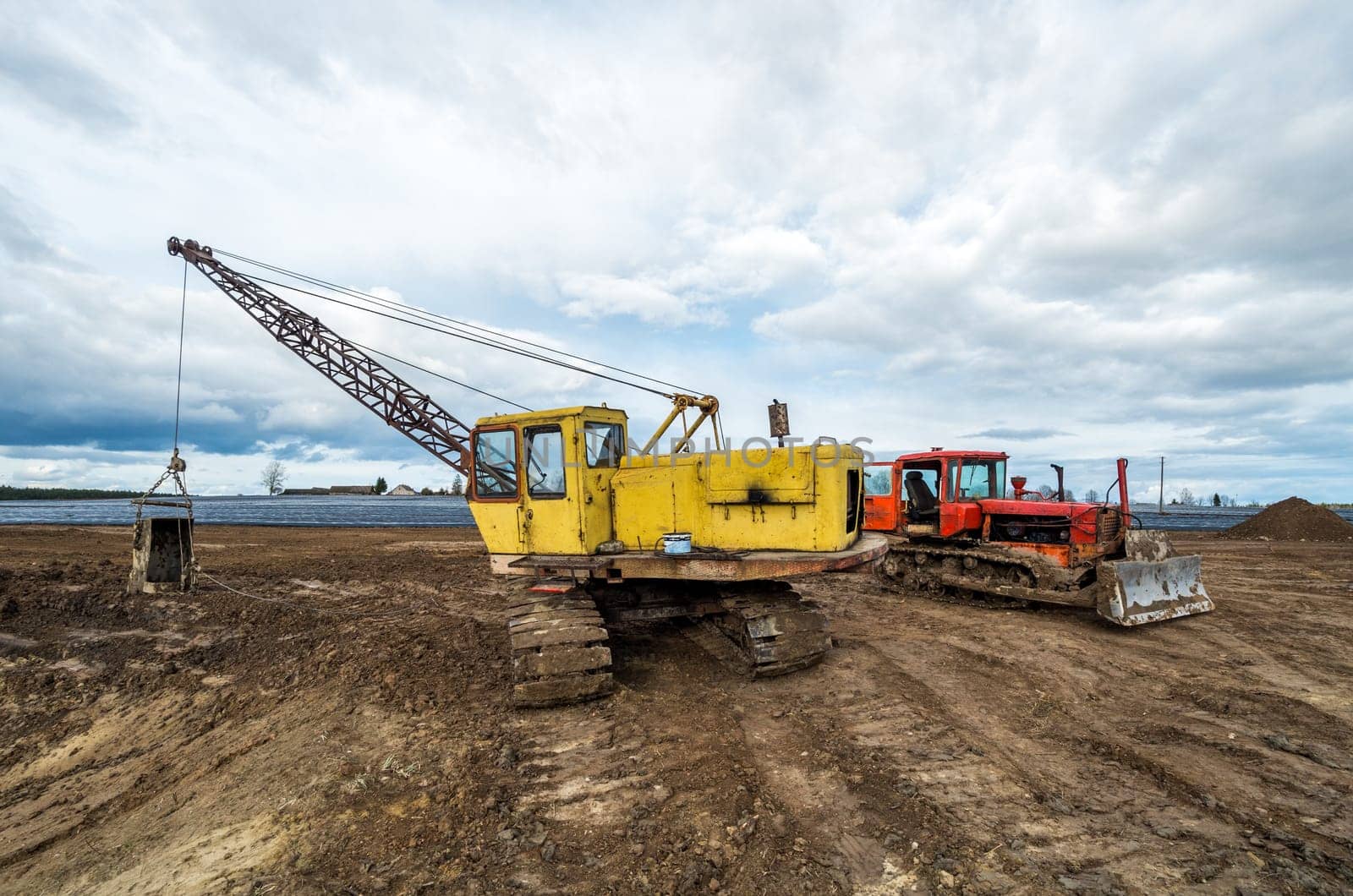 The excavator and old red tractor in the field