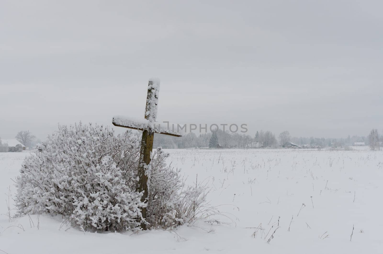 Old weathered wooden catholic cross on a snowy meadow
