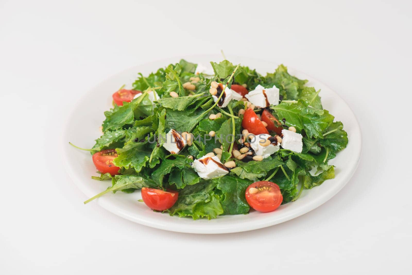 Green salad with vegetables: greens, arugula, tomato, cheese pine nuts and sauce