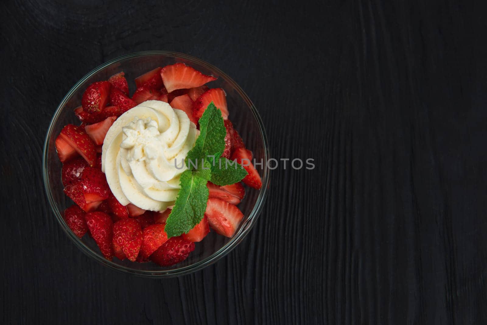 Strawberry with cream decorated with mint leaf on black wooden background