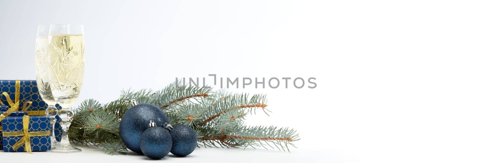 Still life with two champagne flutes, gift boxes and Christmas decoration with fir tree branch on white background with copy space. Christmas and New Year shopping. Greeting card