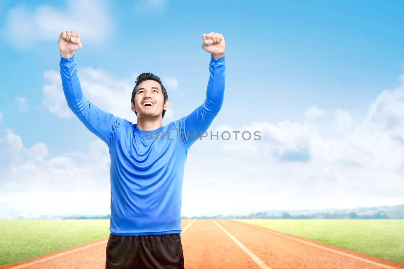 Asian runner man with excited expression after a run on the running track with a blue sky background
