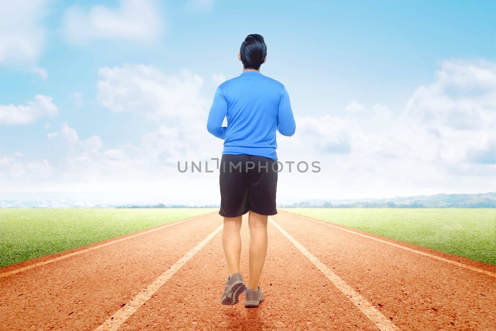 Rear view of Asian runner man running on the running track with a blue sky background