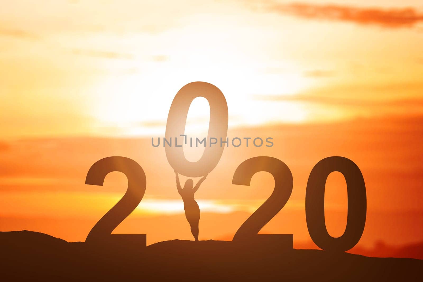 Silhouette of businesswoman put 2020 on the top of the hill with a sunset sky background. Happy New Year 2020